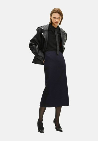Giacca da biker in pelle nera, camicia nera aderente e gonna a matita blu navy slim. Tacchi alti neri e collant neri trasparenti completano il look.