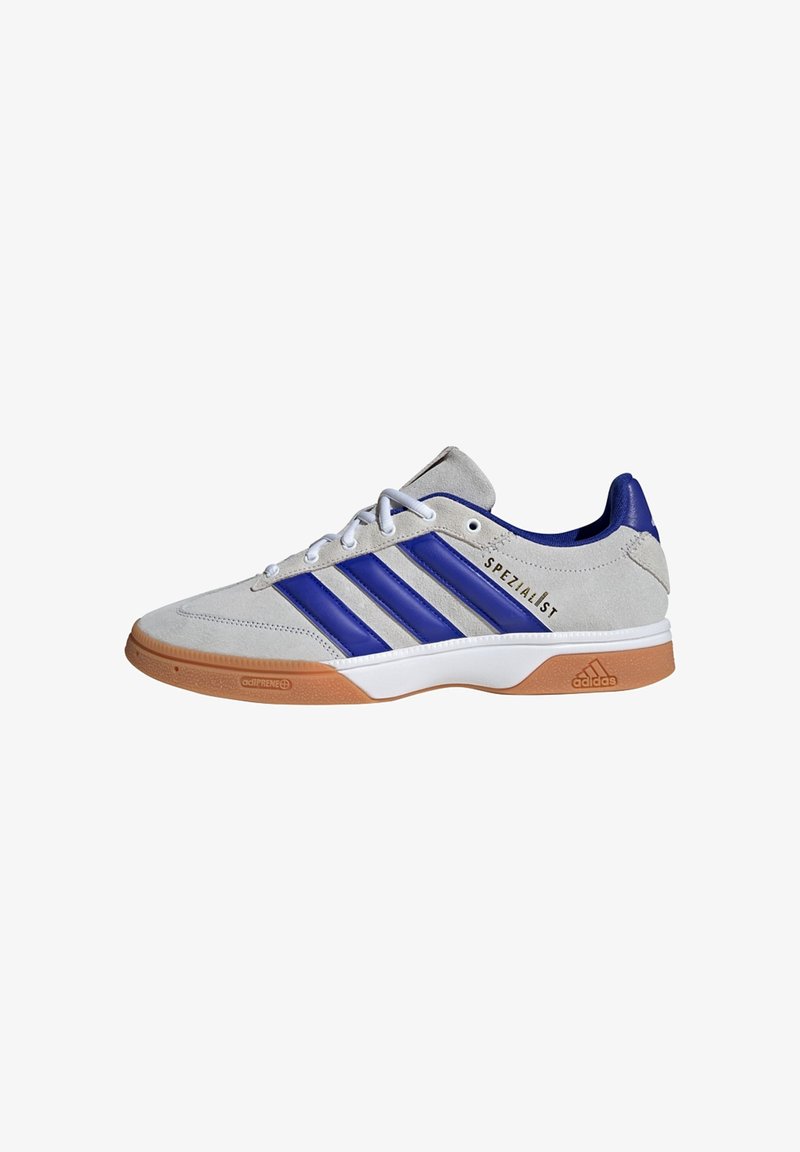 Zapatilla de ante gris con acentos de cuero azul y tres rayas azules. Presenta una suela de goma y "SPEZIALIST" en negro en el costado.