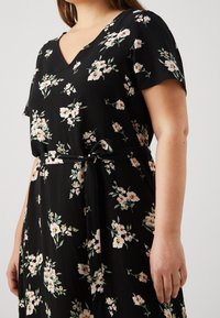 Robe noire à fleurs avec un décolleté en V, des manches courtes et une ceinture en tissu. Présente des fleurs roses et blanches avec des feuilles vertes sur l'ensemble du matériau.