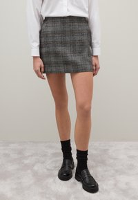 Graues kariertes Minirock mit maßgeschneidertem Schnitt, ausgestattet mit einem Bund und klaren Linien. Kombiniert mit schwarzen Slippern und strukturierten Socken.