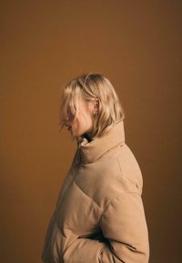 Beżowa kurtka puchowa z korduroyu z wysokim kołnierzem i subtelnym pikowaniem. Miękka faktura, z zapięciem na zamek błyskawiczny z przodu i bocznymi kieszeniami.