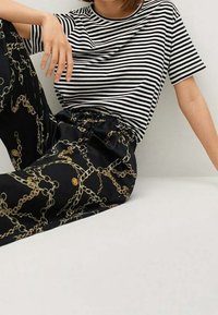 Persoon zittend in een zwart-wit gestreepte short-sleeve shirt en zwarte broek met een gouden kettingpatroon.