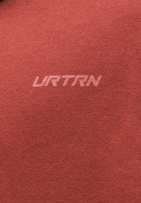 Gros plan d'un tissu rouge avec le texte « URTRN » imprimé en une teinte légèrement plus claire au centre.