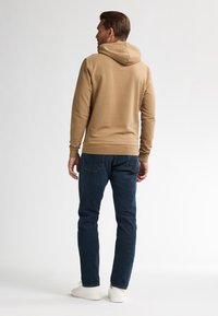 Felpa beige con tasca a marsupio frontale, polsini e bordo a coste. Abbinata a jeans blu scuri e sneakers bianche, vista da dietro.
