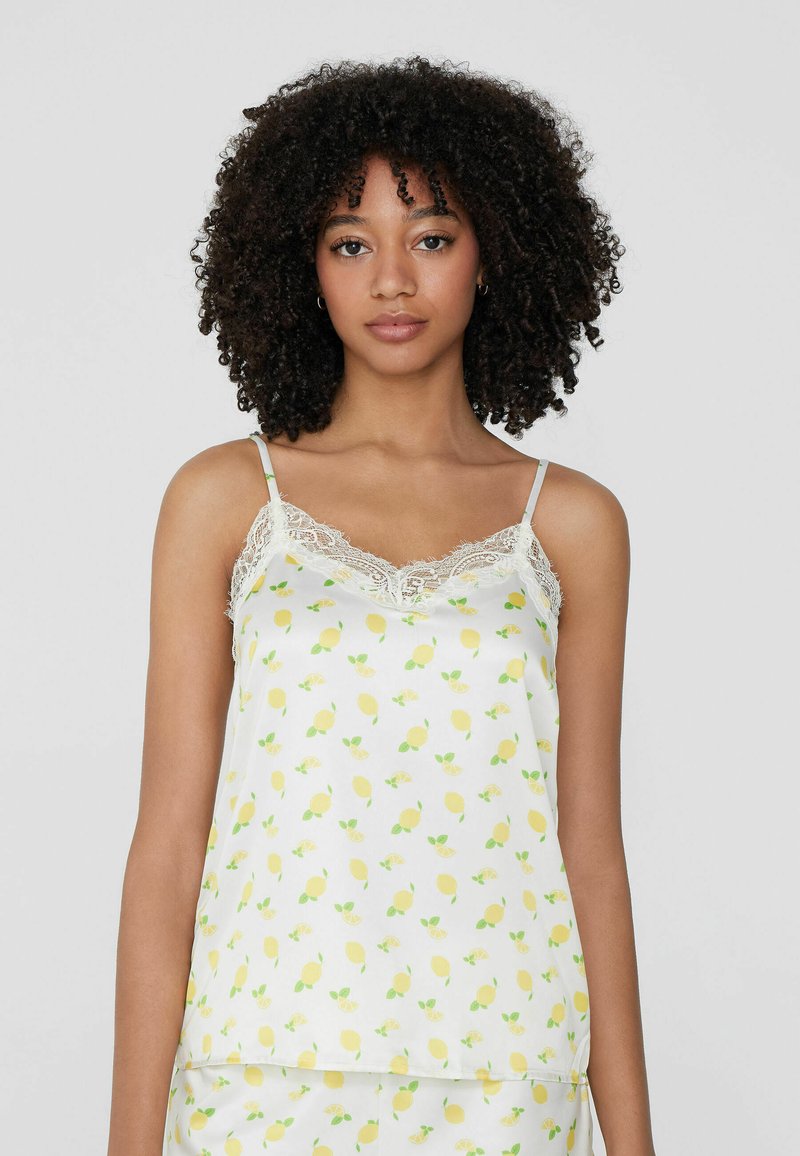 Camisola blanca con estampado de limones, borde de encaje y tirantes finos, que cuenta con una textura suave y un corte relajado.