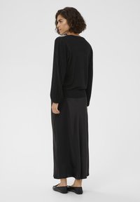 Sort sweater med ribbede lange ærmer, parret med en flydende sort nederdel. Silhuetteret mod en hvid baggrund, teksturen ser blød ud.