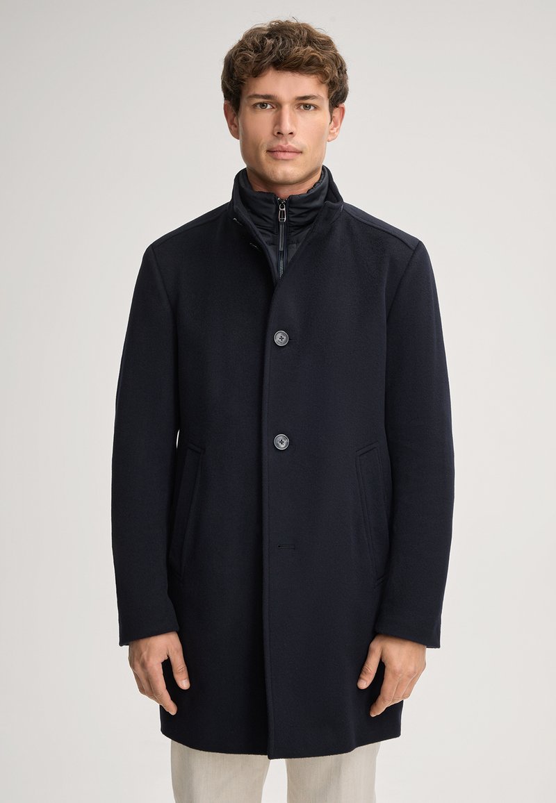 Navyblauer Wollmischgewebe-Mantel mit hohem Kragen, zwei großen vorderen Taschen und drei Knöpfen. Verfügt über ein schlankes, minimalistisches Design.