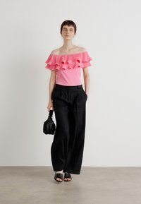 Top rosa sin mangas con detalles de volantes, combinado con pantalones sueltos negros. Incluye un pequeño bolso negro y sandalias negras planas.