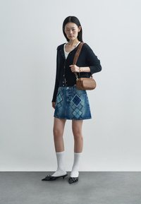 Denimseelik sinise teemantmustriga, must soonikuga kardigan, valged sokid ja mustad teravate otstega kingad. Pruun risti üle keha kantav kott reljeefse tekstiga.