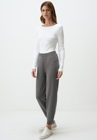 Graue Jogginghosen mit elastischem Bund, kombiniert mit einem weißen, langärmeligen Ripp-Top. Das Model trägt weiße Sneakers und steht vor einem schlichten Hintergrund.