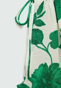 Tkanina s cvjetnim uzorkom u zelenoj i bijeloj boji, s velikim uzorcima lišća. Vrh ima opušteni kroj s podesivim vezicama za zatvaranje.