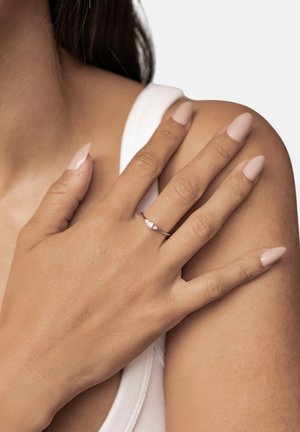 Rose gold ring with three small, clear gemstones, showcased on a hand with natural nails against a light background.
