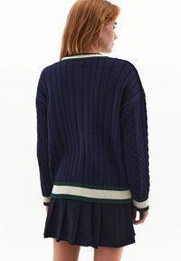 Suéter de canalé azul marino con dobladillo y puños a rayas verdes y crema, con detalles de punto de cable a lo largo de las mangas.