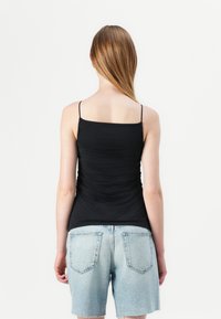 Zwarte spaghetti-top met een vierkante halslijn en dunne schouderbandjes, met een plooidetail aan de achterkant, gecombineerd met lichtblauwe denimshorts.