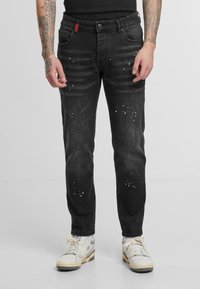 Jeans de mezclilla negra con detalles desgastados y acentos moteados. Cuenta con cinco bolsillos, cierre de botón y un corte slim moderno.