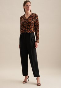 Blusa con stampa leopardata in arancione e nero, design a V, abbinata a pantaloni neri a vita alta e sandali neri con tacco alto.