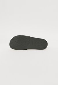 Črne natikače z teksturiranim gumijastim podplatom, ki vsebuje krožno vzorčenje in pravokotni del pete. Čist, minimalističen dizajn.
