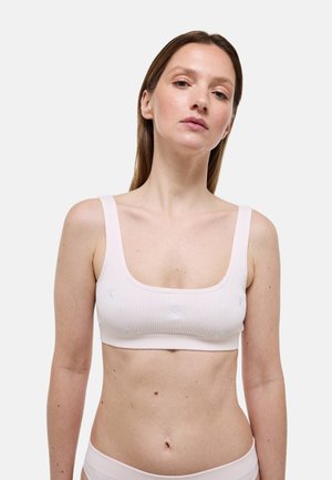 Femme aux cheveux bruns et raides portant un crop top côtelé rose pâle et un bas assorti avec une petite broderie florale blanche.