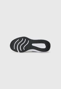 Black rubber shoe sole with a wave pattern, featuring white accents and ridges for traction. Smooth texture and rounded shape.