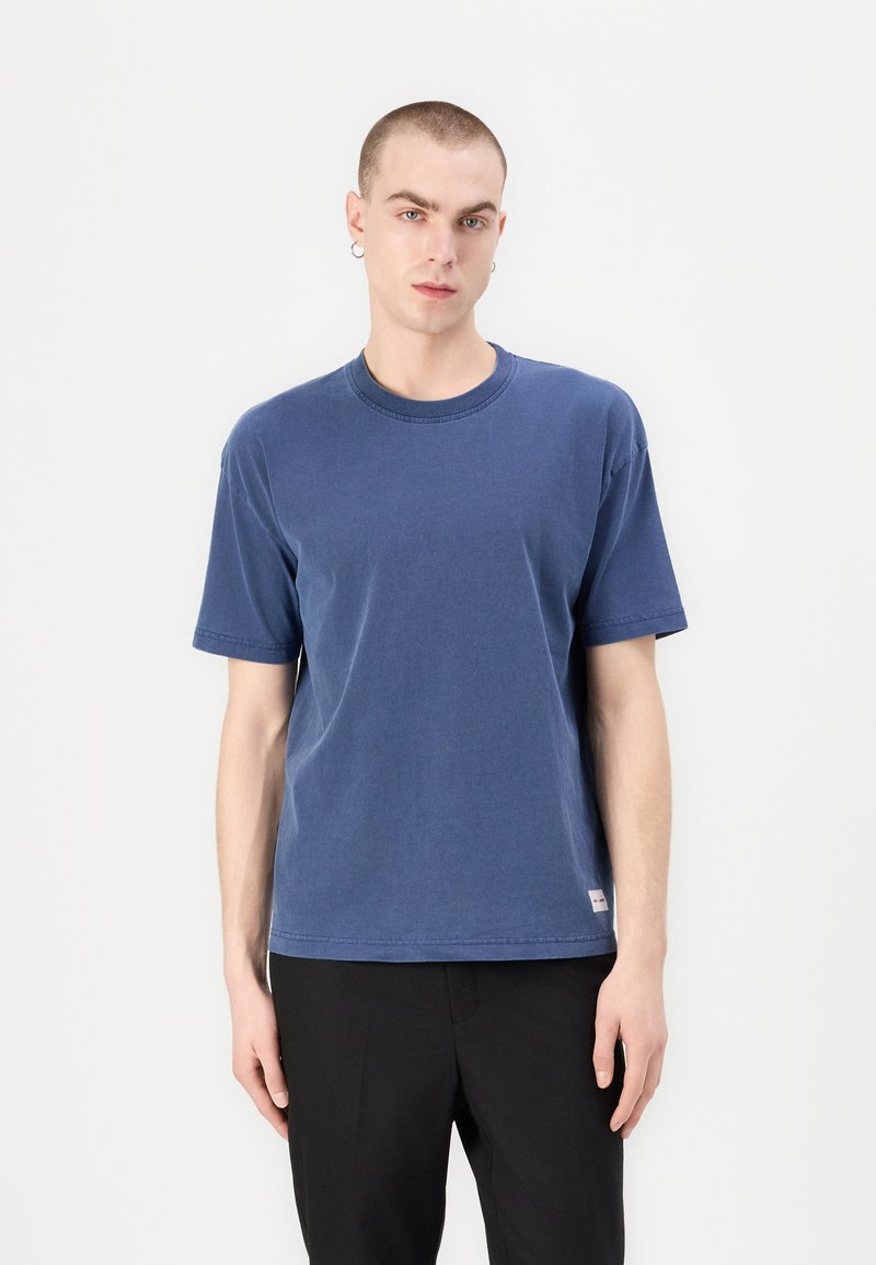 Navy blue cotton t-shirt with short sleeves and crew neck; features a subtle logo tag at the hem; soft texture, relaxed fit.