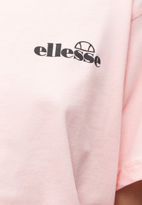 Ροζ ύφασμα με μικρό μαύρο λογότυπο «ellesse» και ημικυκλικό σχέδιο τυπωμένα κοντά στην περιοχή του άνω στήθους.