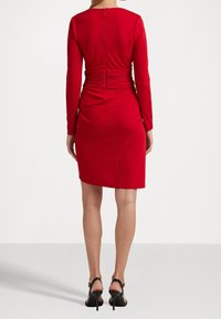 Abito rosso a maniche lunghe con silhouette aderente, caratterizzato da dettagli arricciati sul retro e una cerniera nascosta per la chiusura.