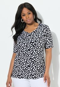Schwarzes und weißes Polka-Dot-T-Shirt mit kurzem �Ärmel und V-Ausschnitt, aus glattem Stoff hergestellt, mit lockerer Passform und gewölbtem Saum.