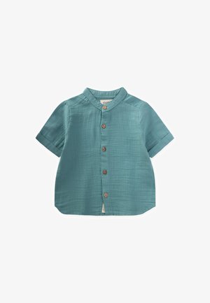 Camicia a maniche corte con bottoni di colore teal, realizzata in tessuto leggero e dalla texture liscia. Presenta un colletto a bande e cinque bottoni in legno.