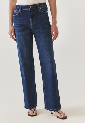 Donkerblauwe wijde jeans van denim, met een hoge taille, voorzakken en contrasterende stiksels. Gestyled met zwarte slippers.