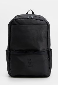 Černý nylonový batoh s hladkou texturou, dvojitým zipem, předním kapsou a logem ve spodní části. Pevné horní madlo pro nošení.