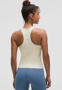 Jasna kremowa sportowa koszulka bez rękawów z designem typu racerback i bezszwową konstrukcją. Można ją zestawić z niebieskimi legginsami do aktywności fizycznej.