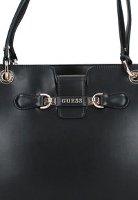 Sac à main synthétique noir avec deux poignées, arbore un logo de marque en ton doré et du matériel assorti, texture lisse et design structuré.