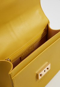 Gelbe strukturierte Lederhandtasche mit einem Reißverschlussfach im Inneren und einem Verschluss aus goldfarbenem Metall. Innenfutter in einer passenden Farbe.
