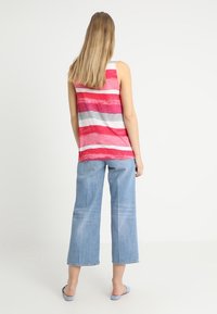 Mouwloze tanktop in roze en grijs gestreept, gecombineerd met lichtblauwe wijde jeans. Zachte stof, relaxed fit, casual ontwerp.