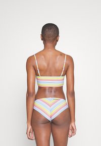 Completo bikini a righe composto da top bralette e slip coordinati. I colori includono rosa, giallo e blu in un motivo a zigzag. Tessuto morbido.