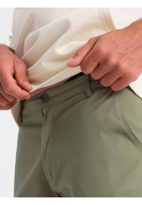 Olivové kalhoty vyrobené z bavlněné směsi s knoflíkovým uzávěrem, mající ploché přední kapsy a hladkou strukturu. Viditelný pas a lem.
