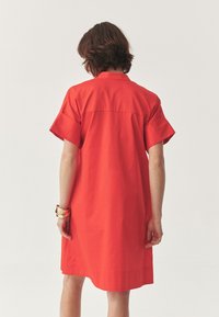 Short-sleeve red dress with a straight cut, button-down collar, and stitched detailing on the back. Smooth cotton fabric.