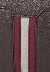 Cuir texturé marron avec des rayures verticales contrastées en bordeaux et crème. Les détails de couture visibles renforcent la structure du design.