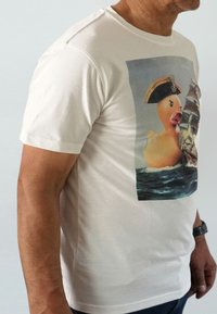White cotton t-shirt featuring a printed graphic of a rubber duck in a pirate hat next to a ship on a sea background. Short sleeves.