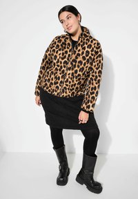 Giacca trapuntata con stampa leopardata e zip frontale, gonna nera, collant neri e stivaletti neri chunky. Tessuto testurizzato e motivi distintivi.