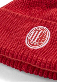 Bonnet rouge en tricot avec texture côtelée, présentant un logo en relief blanc et rouge comprenant "ACM" et "1899". Matière douce, design avec revers.