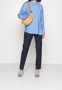 Blau-weiß gestreiftes Langarmshirt, marineblaue Hose, hellblaue Blockabsatzsandalen und eine gelbe Umhängetasche mit einem grünen Riemen.
