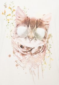 Camiseta blanca con un gráfico de un gato usando gafas de sol y una bufanda estampada, rodeado de ilustraciones florales y toques de salpicaduras.