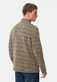 Texturierte braune Jacke mit Stehkragen, die ein gemischtes Garnmuster und eine lässige Passform bietet. Von hinten betrachtet, über Jeans getragen.