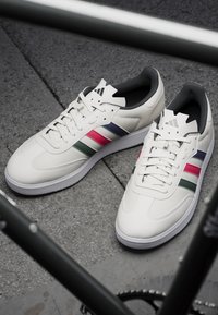 Białe skórzane sneakersy z wielokolorowymi paskami (zielonym, różowym, granatowym) po bokach, z teksturowaną podeszwą i wzmocnionymi oczkami.