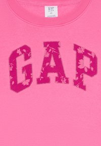 Sweatshirt rosa com o logótipo "GAP" em padrão floral em rosa mais escuro com detalhes em costura prateada. Textura suave, design de gola redonda.