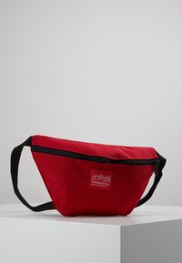 Red fabric fanny pack with a zip closure, black accents, and a logo patch. Compact design with an adjustable strap for secure wear.