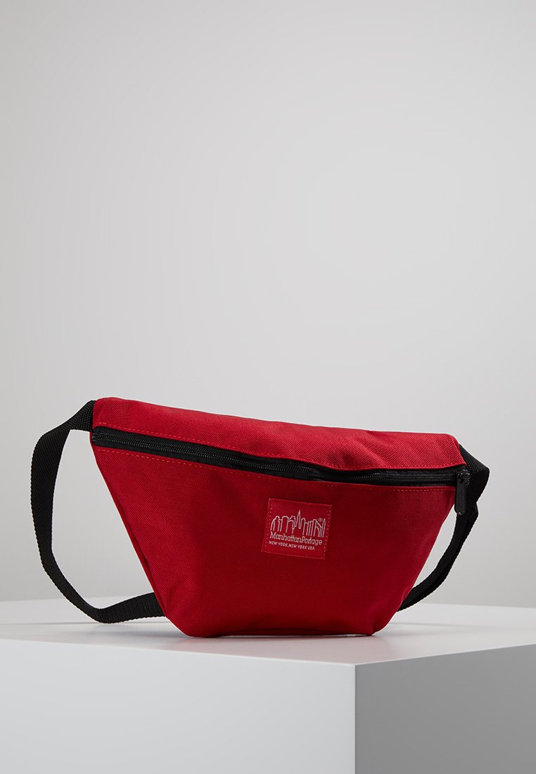 Red fabric fanny pack with a zip closure, black accents, and a logo patch. Compact design with an adjustable strap for secure wear.