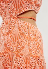 Rochie brodată de culoare portocalie cu modele florale intricate și detalii cu decupaje. Material texturat cu accente împletite la talie.