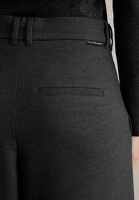 Zwarte op maat gemaakte broek met een visgraatpatroon, een vlakke achterzak en een gladde textuur, voorzien van een riemlusdetail.